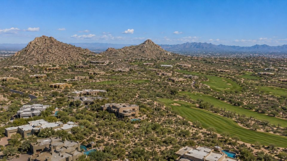 Aerial panorama of a desert golf course community with luxury homes, green fairways and rocky hills