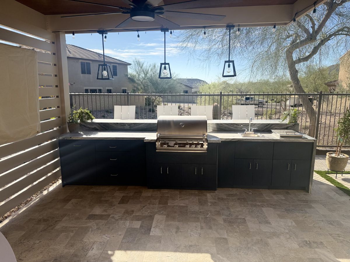 Modern outdoor kitchen with stainless steel built-in grill, marble countertops and patio in sunny backyard
