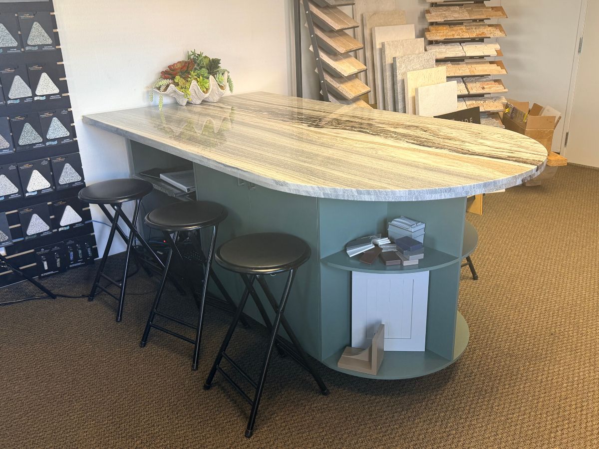 Kitchen island showroom with marble-look quartz countertop, green base, three black stools and tile samples