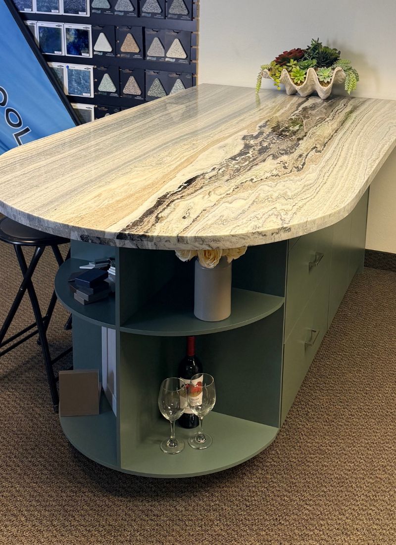 Polished granite countertop island with swirling veining, curved green base, open wine storage and succulent decor
