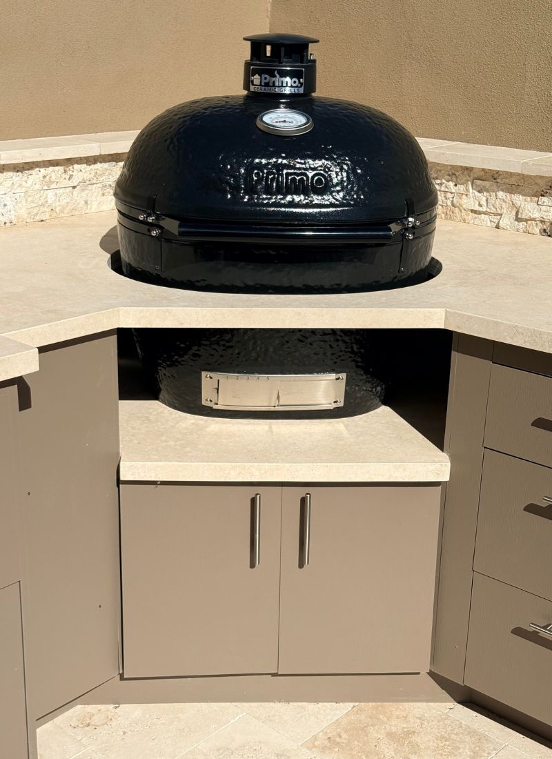 Primo ceramic kamado grill built into outdoor kitchen with stone countertop and storage cabinets
