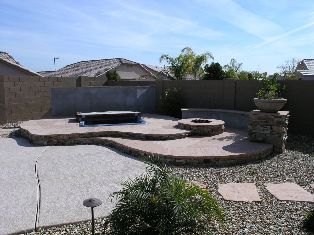Modern multi-level backyard patio with stone seating, built-in fire pit, spa cover and desert rock landscaping