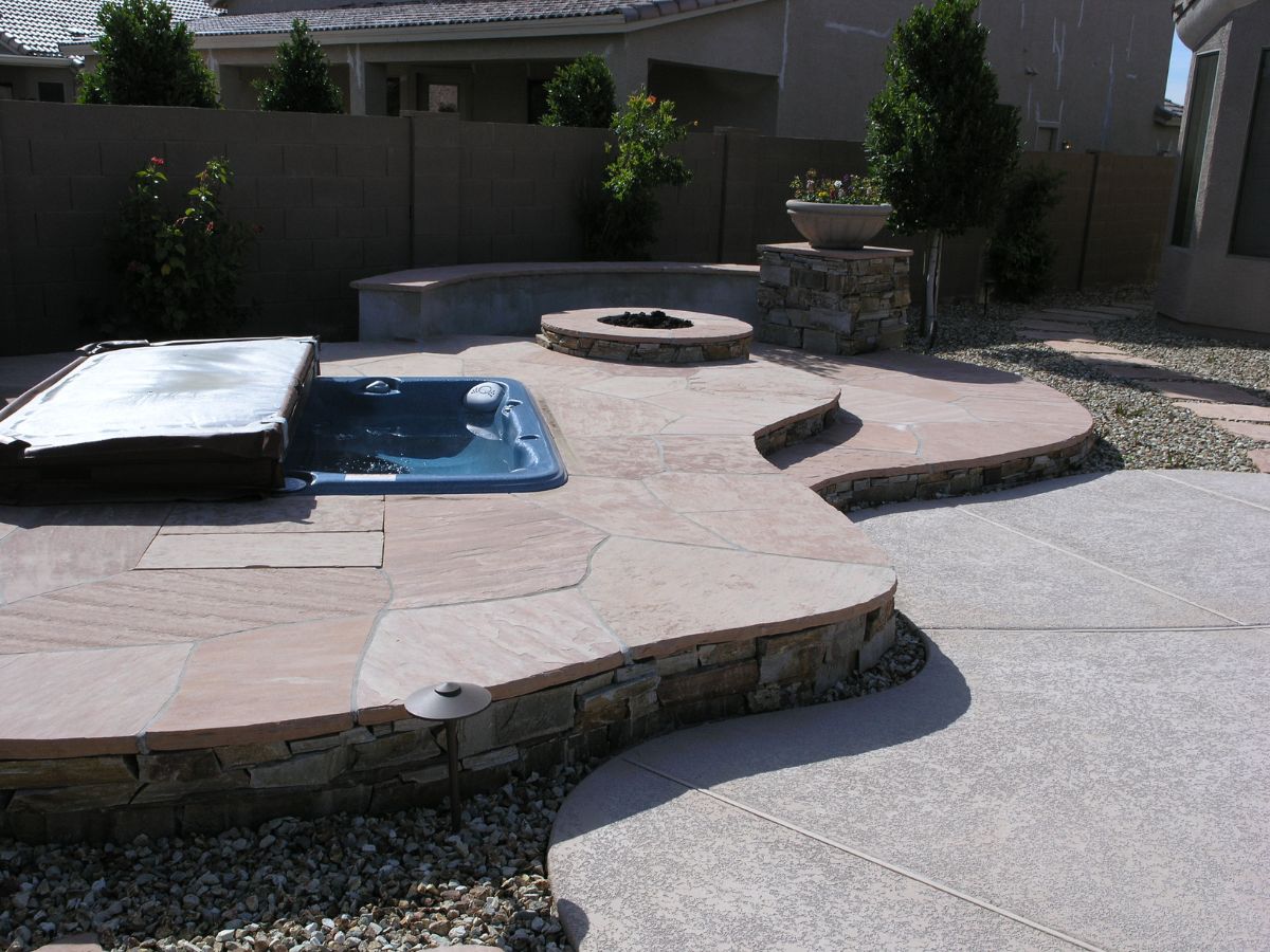SEO-optimized alt text: Modern backyard patio with built-in blue hot tub, curved stone decking, raised fire pit and planter