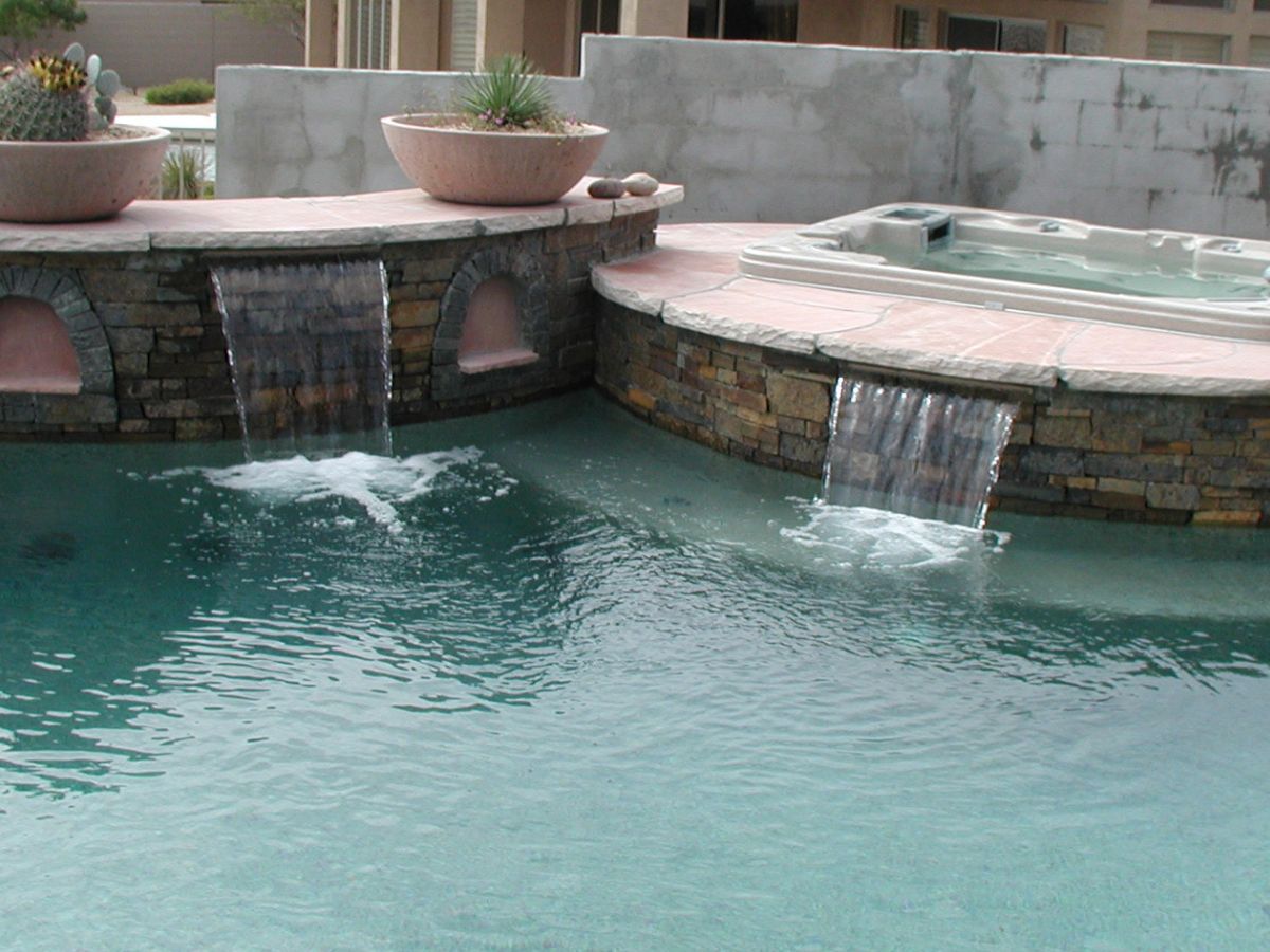 Luxury backyard pool with stone waterfall spillways and attached raised spa/hot tub