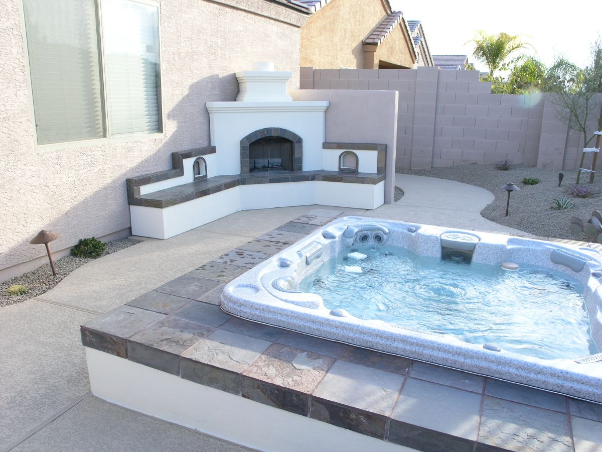Hot tub spa in backyard patio with built-in outdoor fireplace, tiled seating and desert landscaping