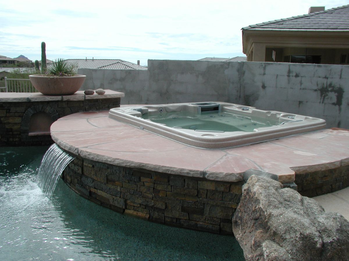Luxury backyard spa and hot tub integrated into pool with stone surround and waterfall spillover