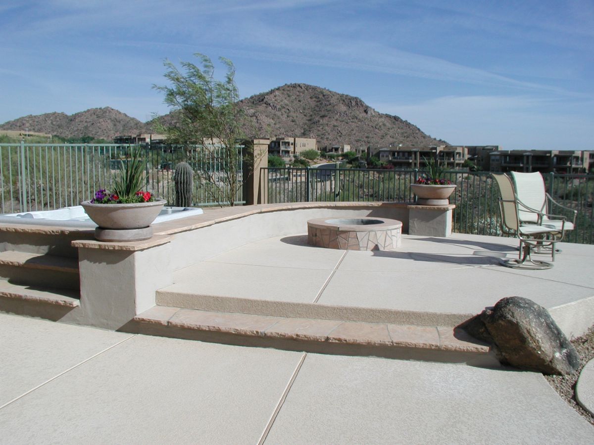 Outdoor patio with round fire pit in desert mountain setting, potted planters and seating