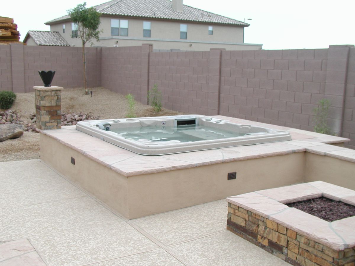 Backyard raised hot tub spa with stone surround and fire pit on patio, desert landscaping and block wall
