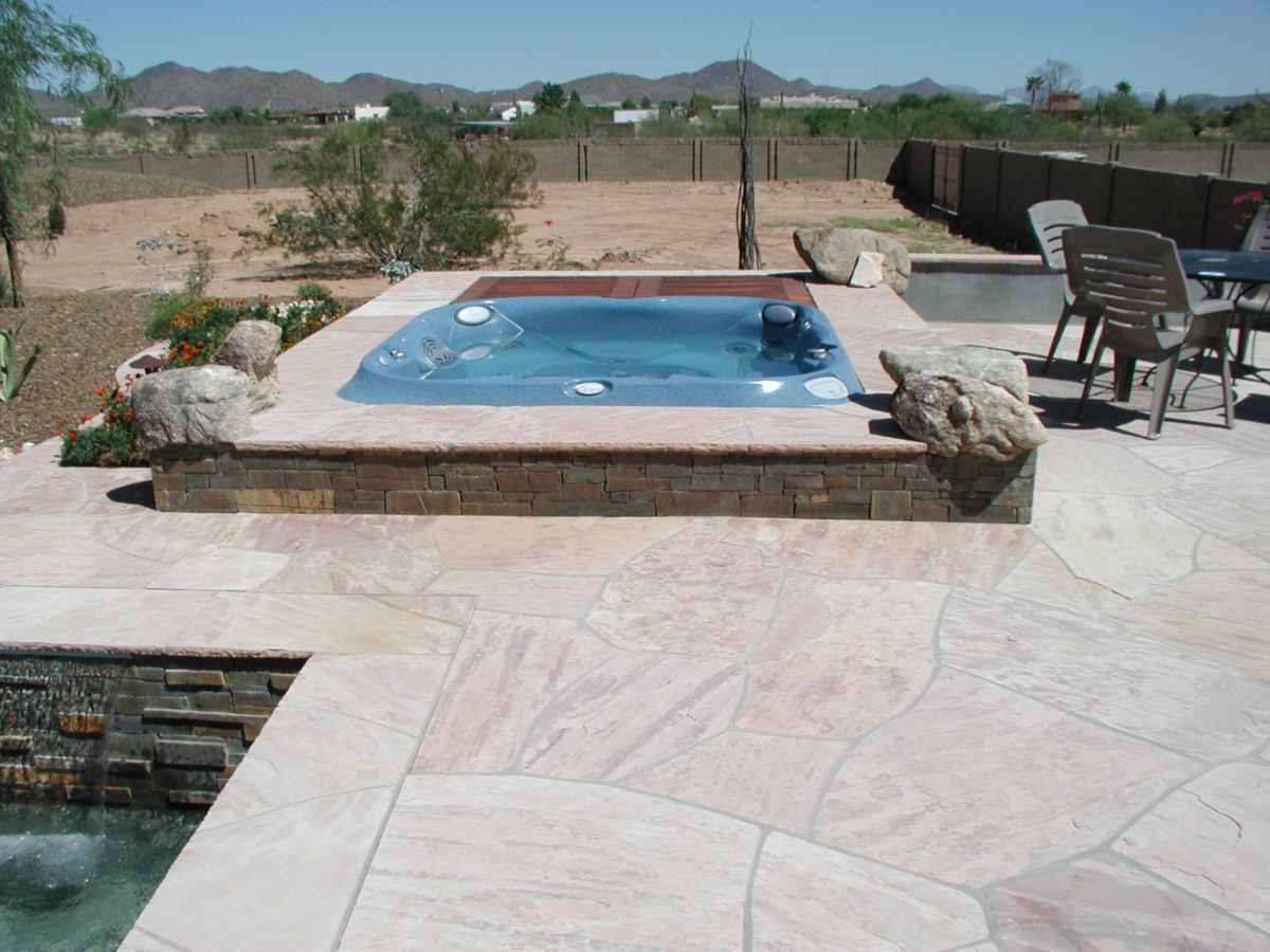 Built-in blue spa hot tub on flagstone patio in desert backyard with stone coping and mountain views