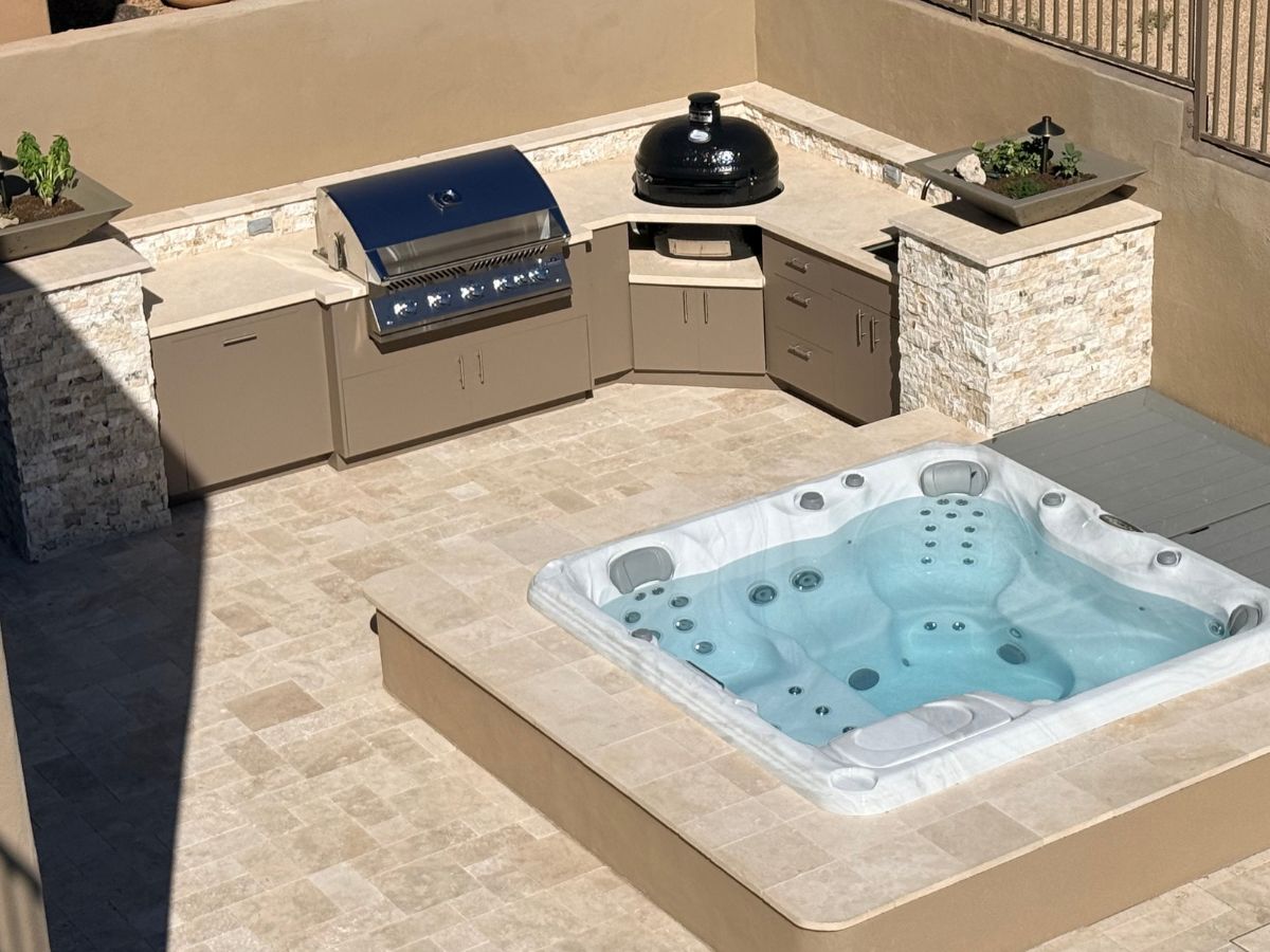 Luxury backyard outdoor kitchen with built-in spa hot tub, stainless steel gas grill and travertine tile patio.