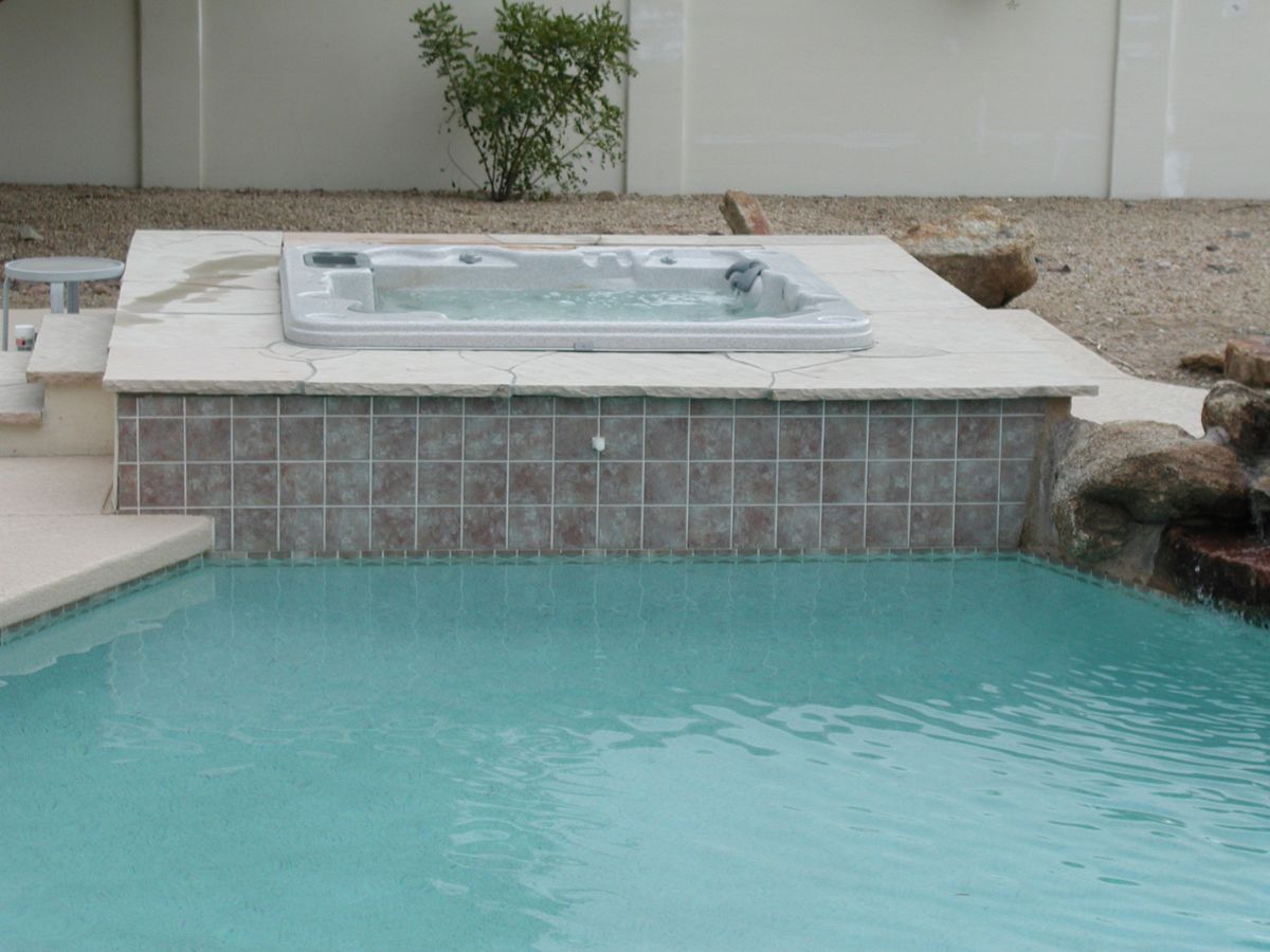 Backyard swimming pool with raised tiled spa/hot tub, stone deck and turquoise water, rock landscaping.