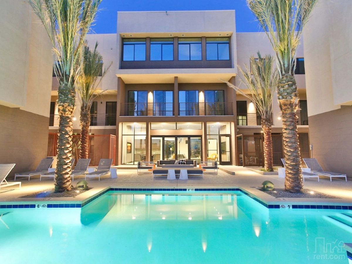 Modern luxury apartment courtyard with illuminated swimming pool, palm trees and lounge seating