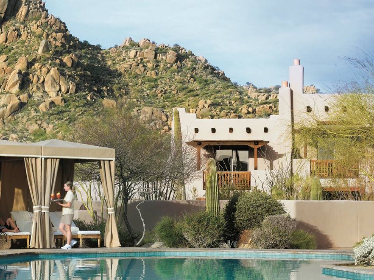 Desert resort pool with cabana and server carrying drinks; adobe hotel and rocky mountain backdrop
