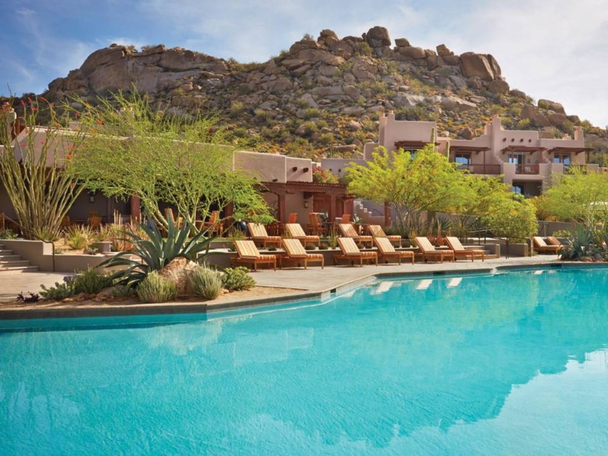 Luxury resort pool with wooden lounge chairs, desert landscaping and rocky hillside backdrop