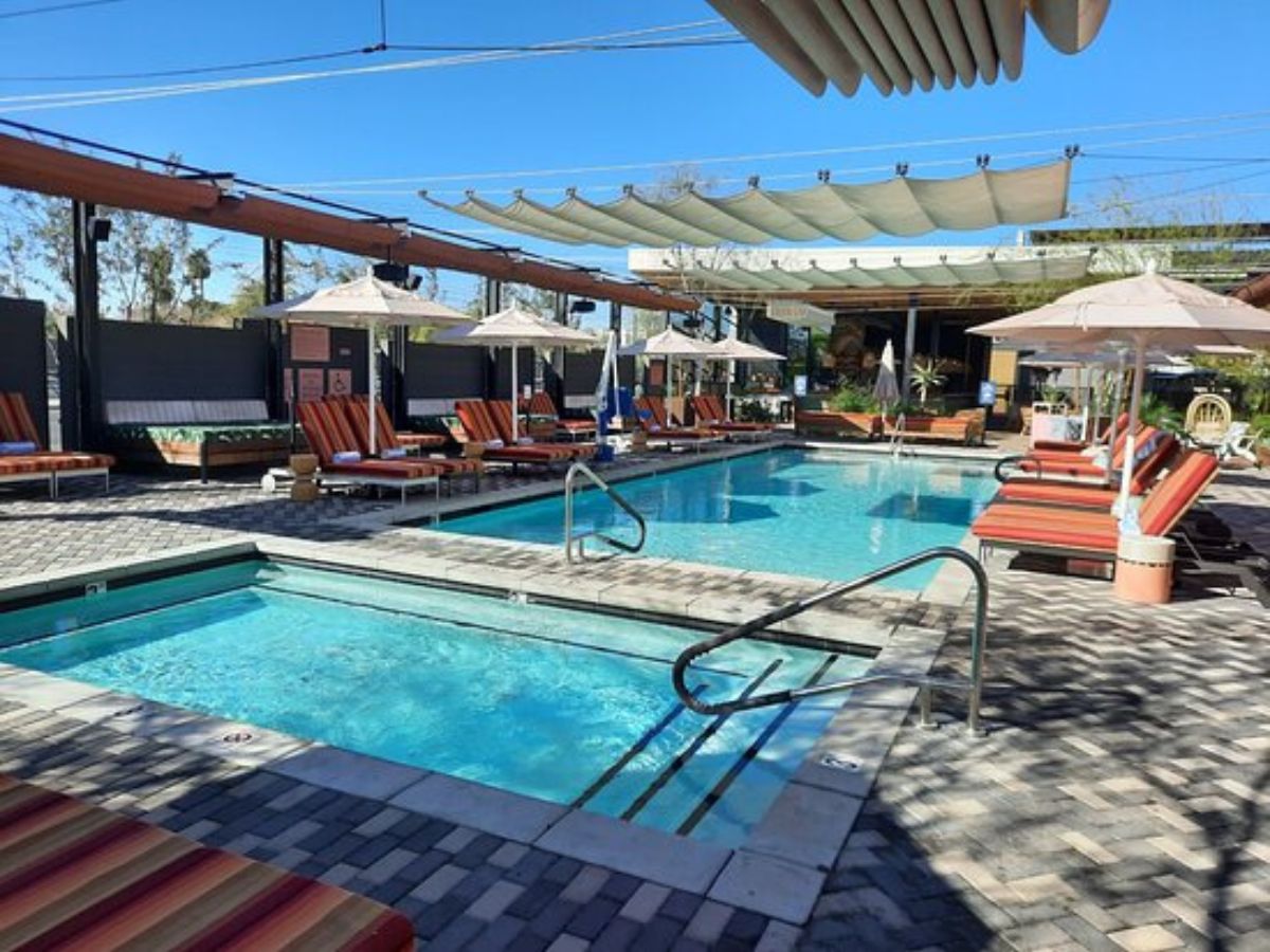 Resort-style outdoor pool and spa with clear blue water, striped lounge chairs, umbrellas and cabanas