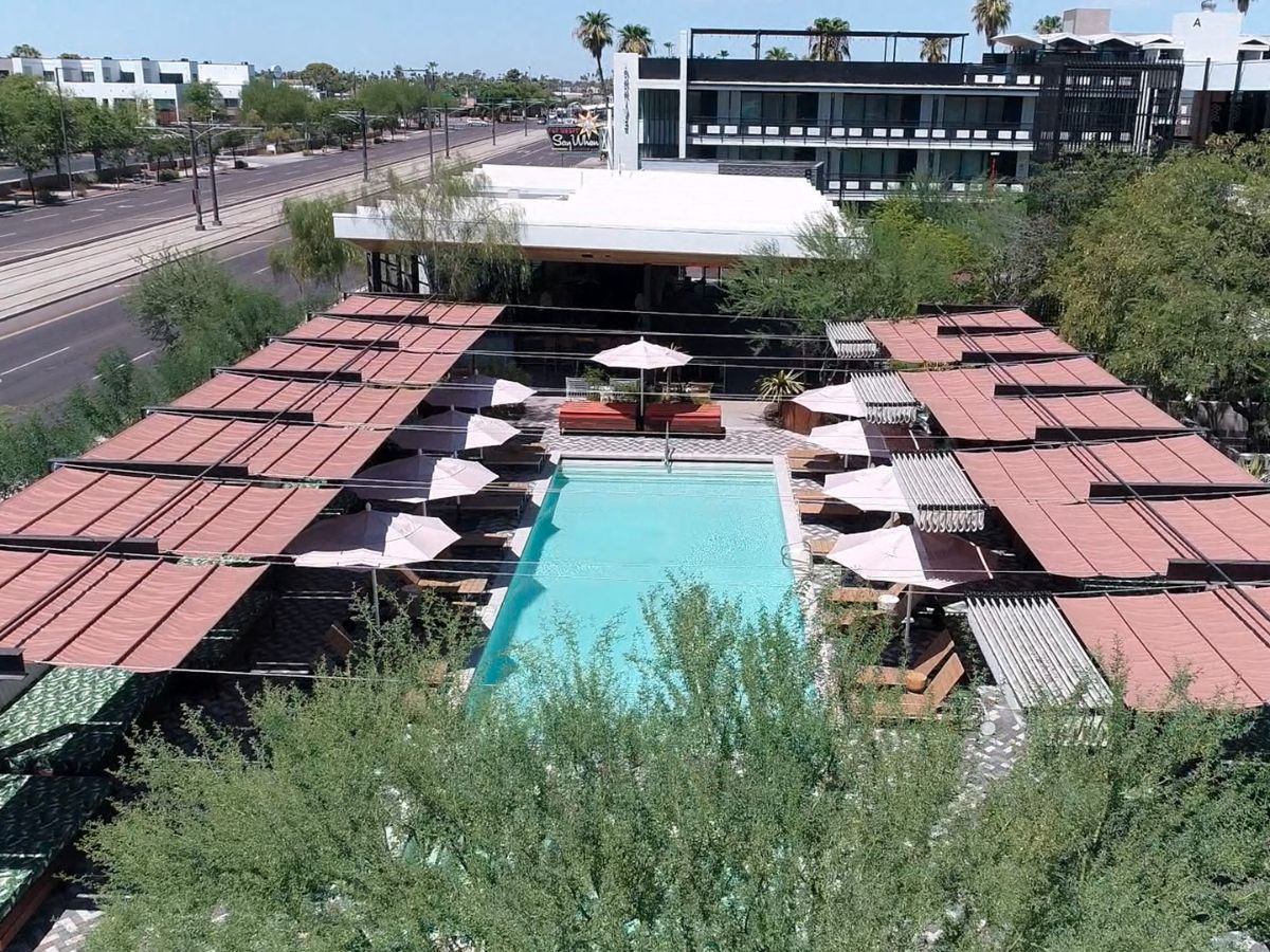 Mid-century modern hotel courtyard pool with turquoise water, lounge cabanas, umbrellas and desert trees