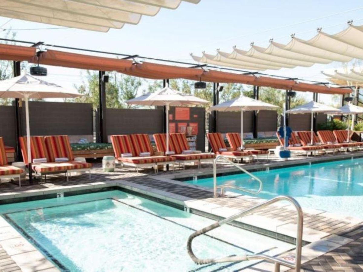 Outdoor resort pool with adjacent hot tub, striped sun loungers, white umbrellas and shaded cabana sails
