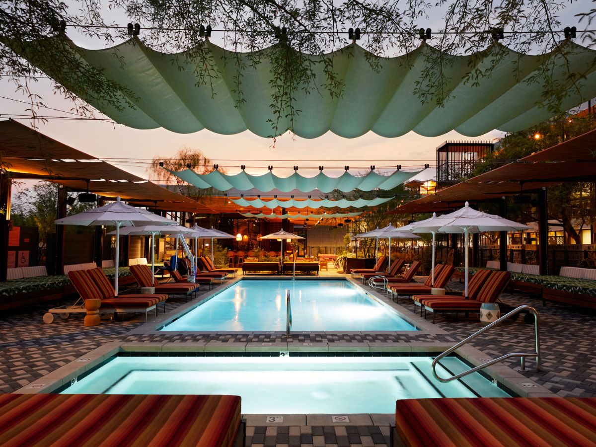 Luxury hotel pool at dusk with striped lounge chairs, white umbrellas and scalloped green shade sails