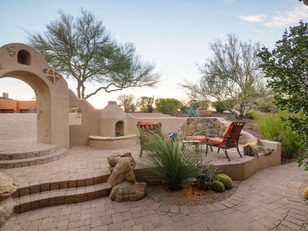 Southwestern adobe patio with arch, paver steps, desert plants, cacti and red-cushion chairs by a kiva fireplace