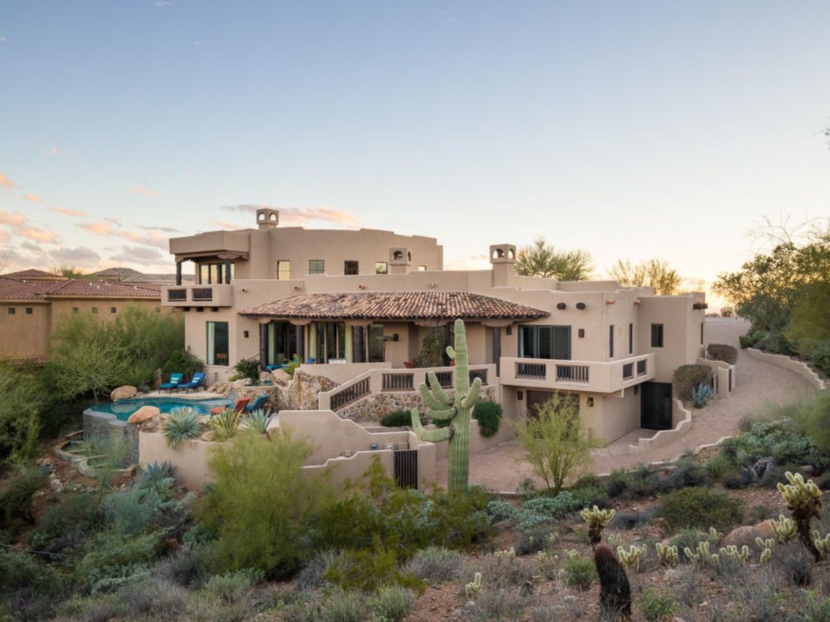 Southwestern luxury desert home with stucco walls, tiled roof, backyard pool and saguaro cactus at sunset