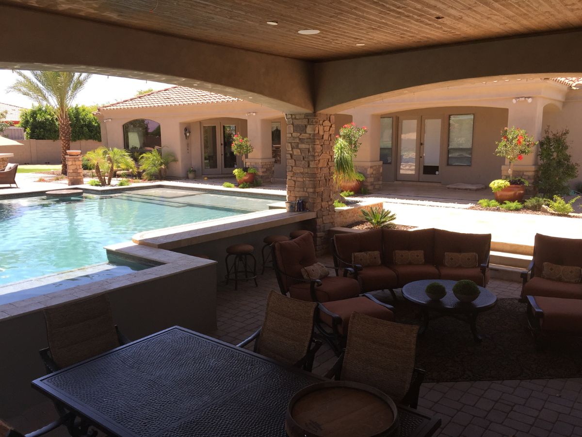 Covered backyard patio with outdoor lounge seating, dining table and swimming pool by stone columns