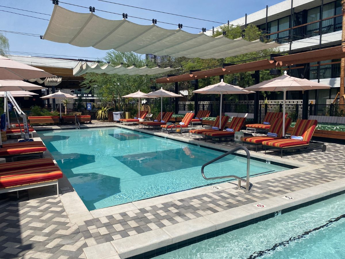 Outdoor hotel pool with striped lounge chairs, umbrellas, overhead shade sails and clear blue water