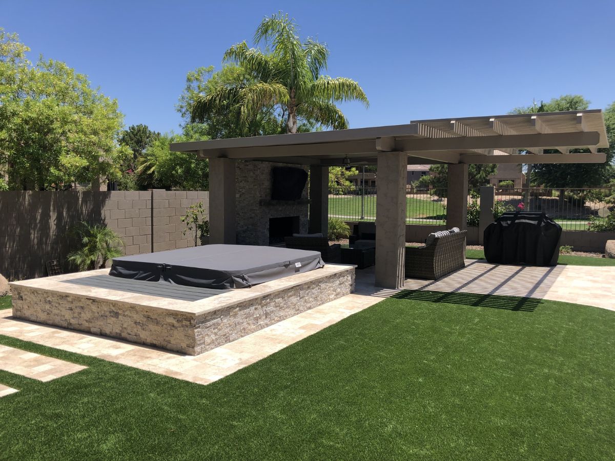 Modern backyard patio with pergola, covered hot tub, stone surround, seating area, outdoor fireplace and artificial turf