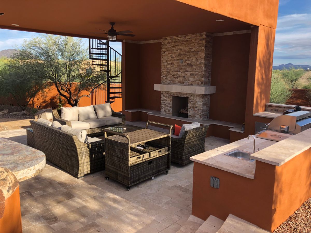 Stylish desert patio with wicker seating, stone fireplace, outdoor kitchen and spiral staircase, mountain view