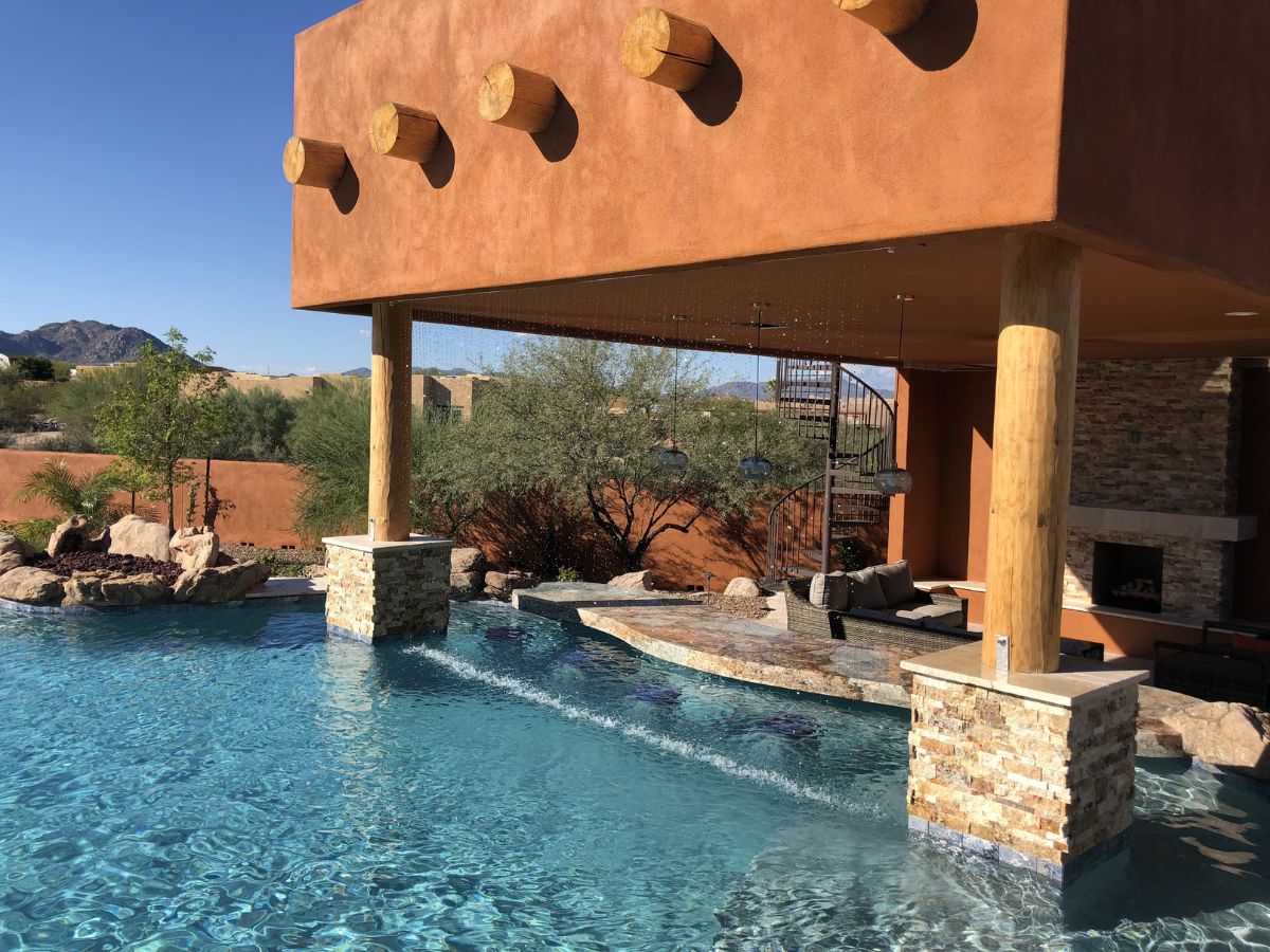 Southwestern backyard pool with swim-up bar, covered patio, wooden vigas, stone columns and spiral staircase