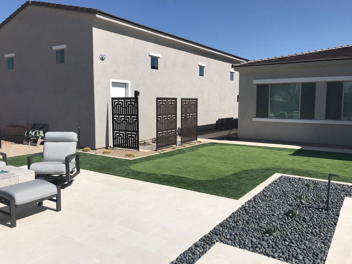 Backyard patio with artificial turf, outdoor lounge chairs, decorative metal privacy screens and river rock garden