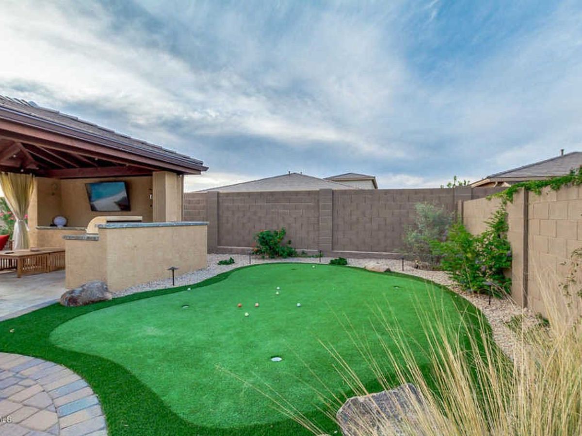 Backyard artificial putting green with covered patio, paver walkway, privacy wall and desert landscaping