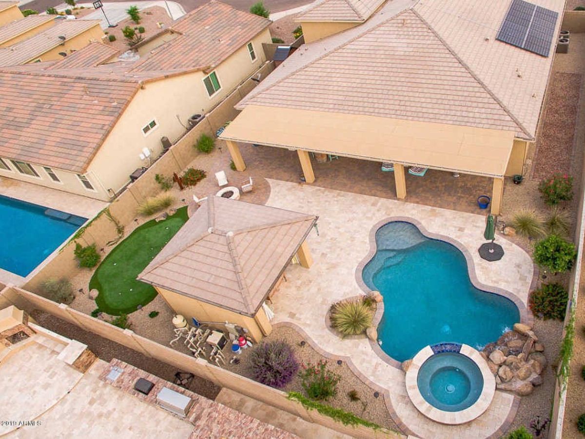 Aerial view of suburban backyard with kidney-shaped pool and spa, covered patio, putting green and desert landscaping