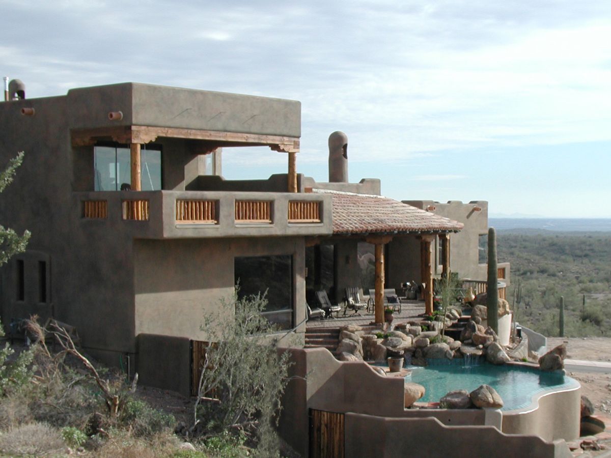 Adobe-style desert villa with covered patio, wooden beams, rocky infinity pool and cacti overlooking desert views