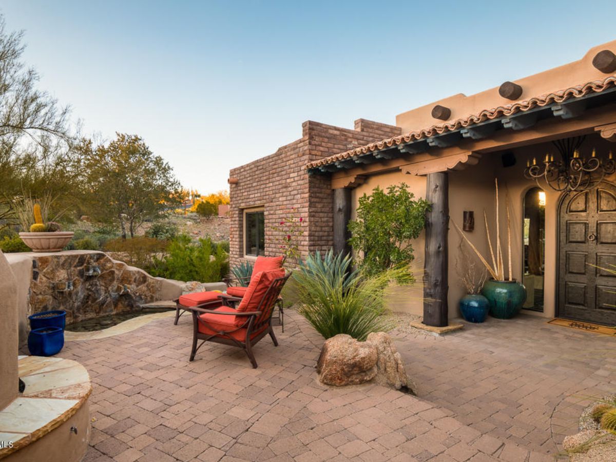 Southwestern adobe patio with red cushioned lounge chairs, paver courtyard, desert plants, fountain and decorative pottery.