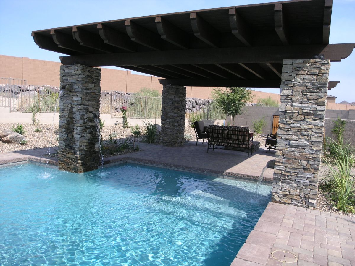 Backyard swimming pool with shaded pergola on stone pillars, cascading water features and patio seating