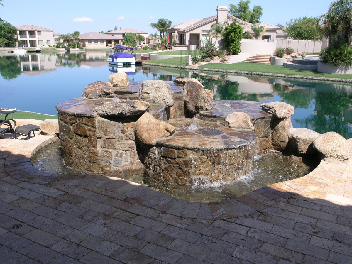 Backyard stone spa with cascading waterfall and lakeside patio, boat and waterfront homes in view