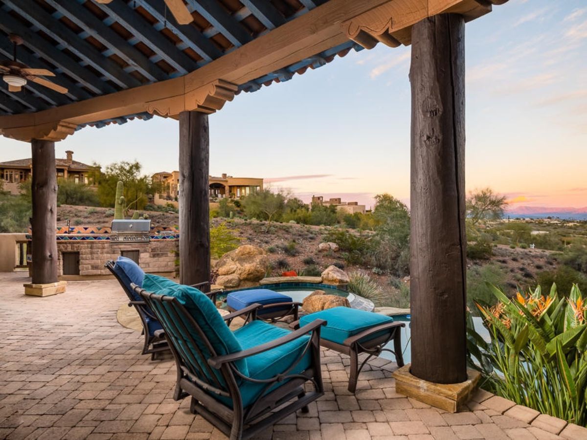 Luxury backyard patio and spa with teal lounge chairs, covered wooden pergola and desert sunset views