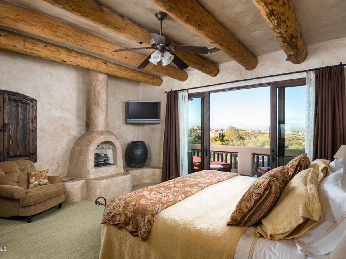 Southwestern luxury master bedroom with kiva fireplace, exposed log beams, bed and balcony with scenic views