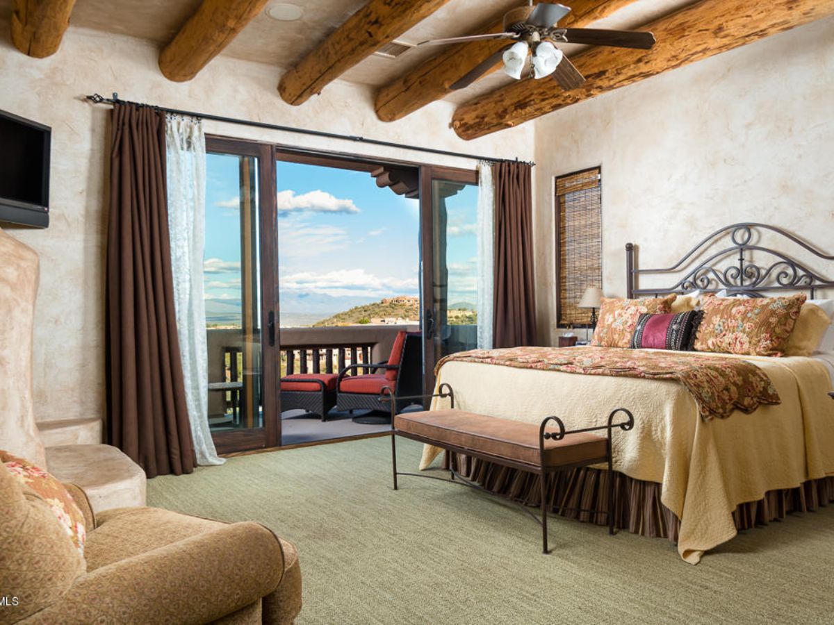 Luxury Southwestern master bedroom with wood-beamed ceiling, king bed and balcony with mountain views