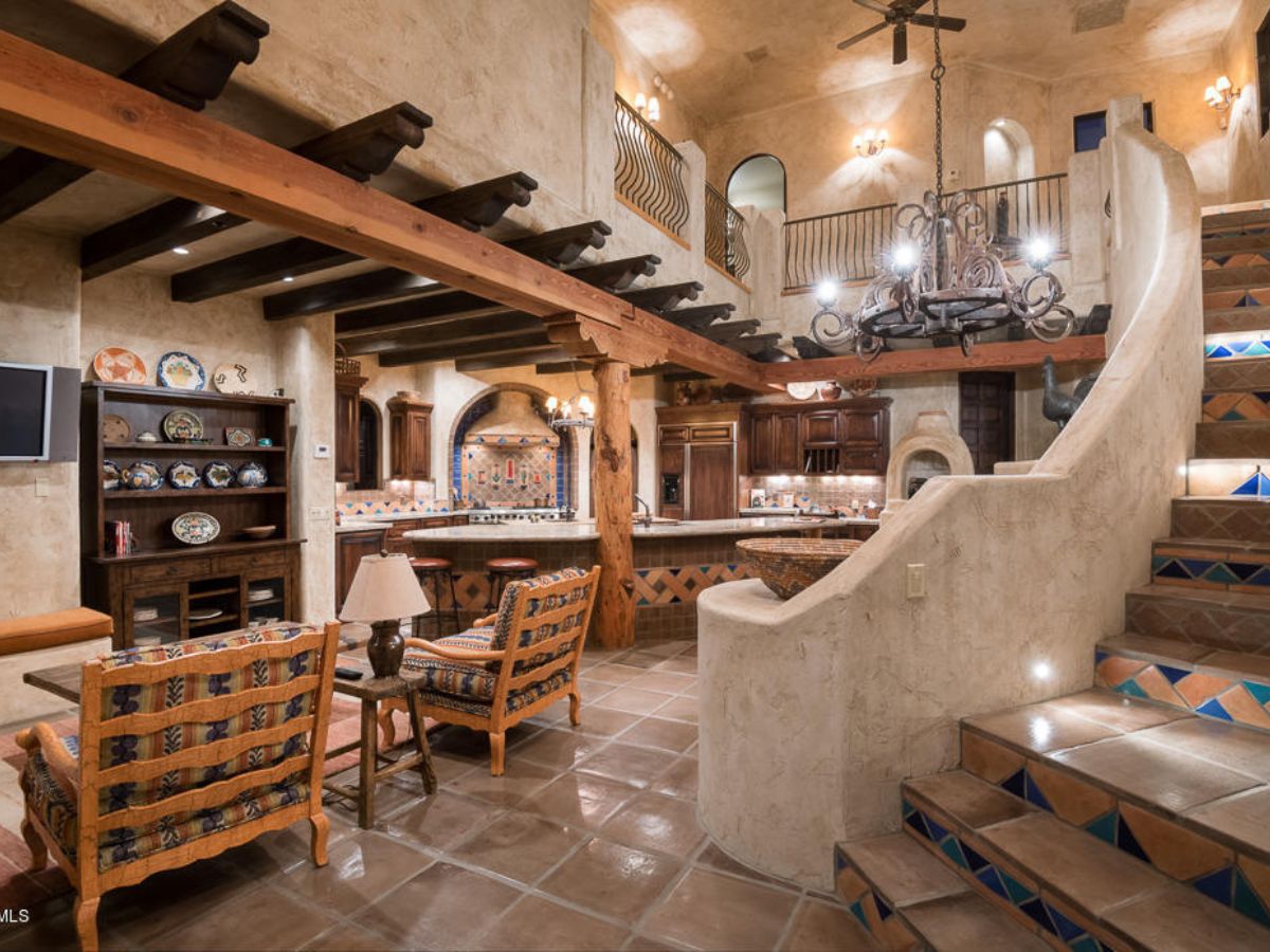 Southwestern open-concept living room and kitchen with exposed wooden beams, tiled staircase and wrought-iron chandelier
