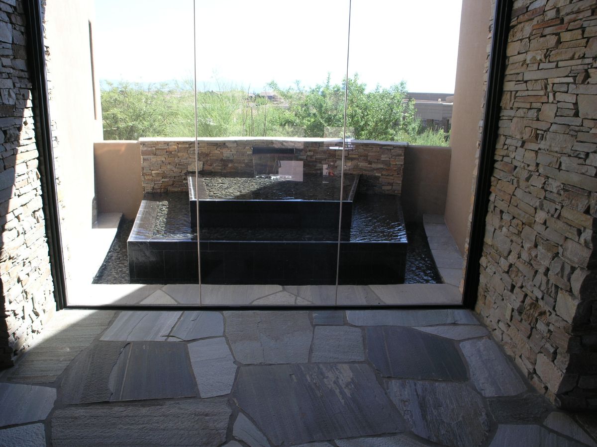 Outdoor stone water feature and reflecting pool behind glass doors, flagstone patio and stacked stone walls