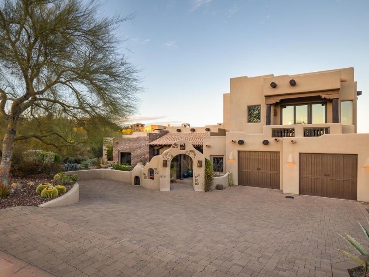 Luxury Southwestern adobe-style home with paved driveway, two wooden garage doors, and desert landscaping