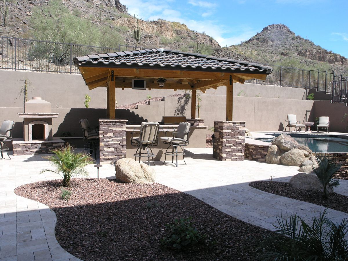 Desert backyard patio with tiled-roof pavilion, outdoor bar and stools, pool, fireplace and mountain backdrop