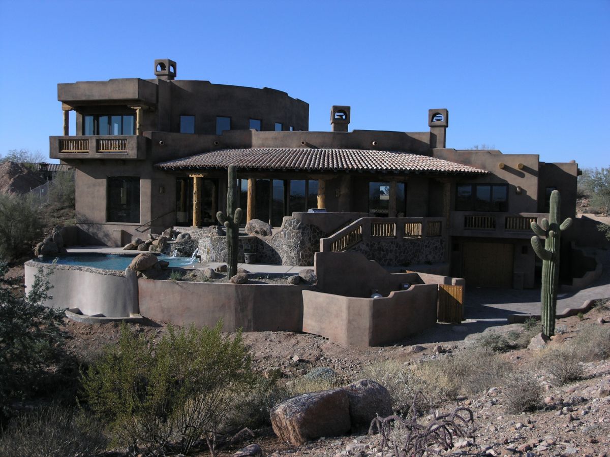 Southwestern adobe luxury home in desert with pool, stone terraces and saguaro cacti under clear blue sky