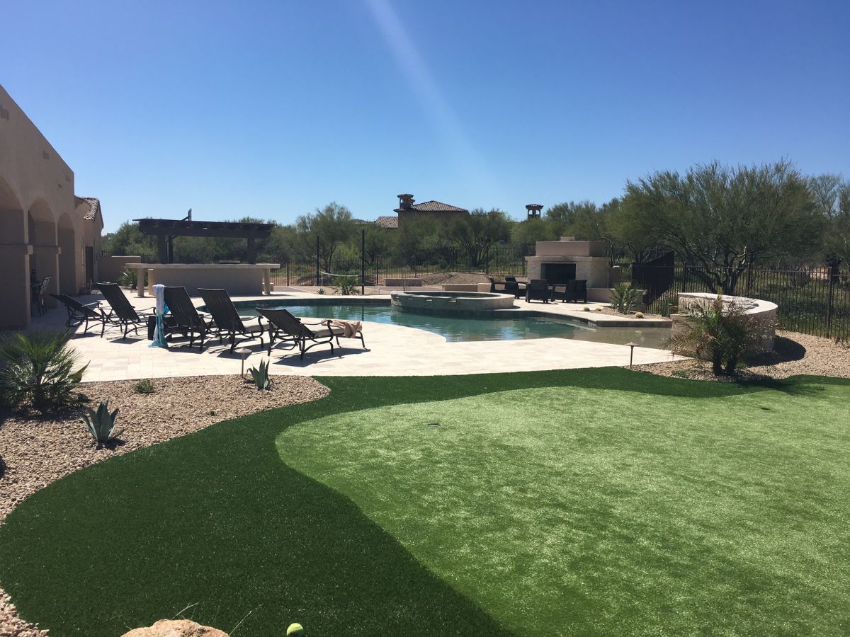 Desert backyard with pool, spa, lounge chairs, pergola and artificial turf putting green under clear blue sky