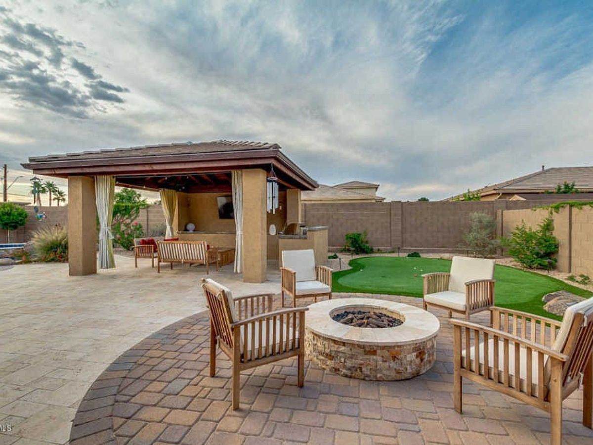 Backyard patio with stone fire pit, wooden seating, covered pergola and putting green