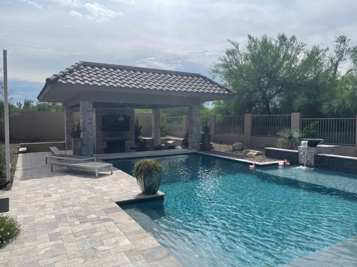 Luxury backyard swimming pool with tiled-roof pavilion, lounge chairs, waterfall feature and desert landscaping