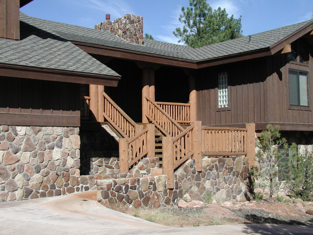 Rustic lodge exterior with stone base and wooden log railing leading to shingled-roof porch