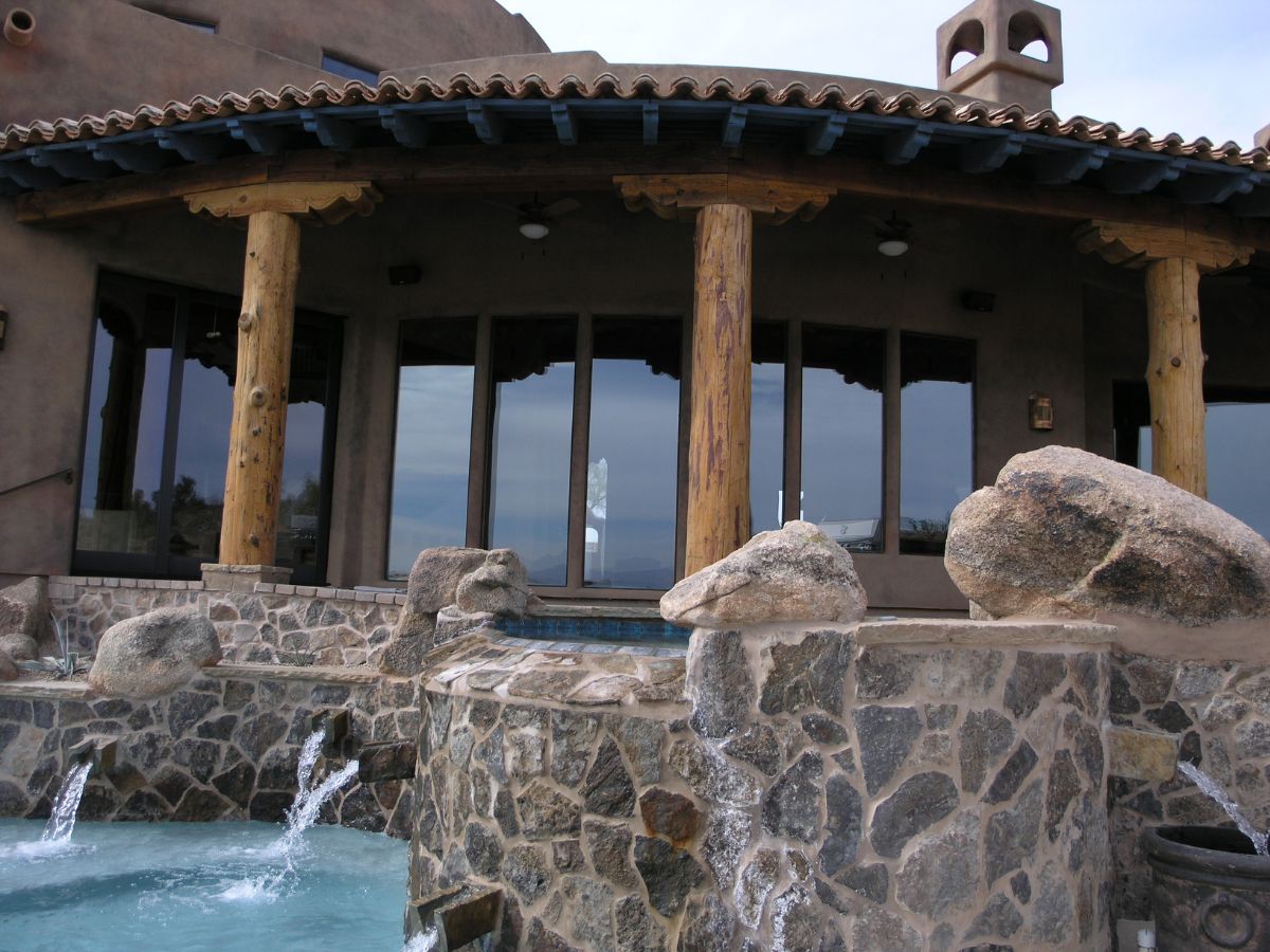 Luxury Southwestern home patio with stone spa and cascading water features, rustic log columns and glass doors