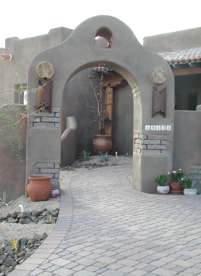 Southwestern adobe archway entrance with curved paver walkway, terracotta pots and xeriscape desert landscaping